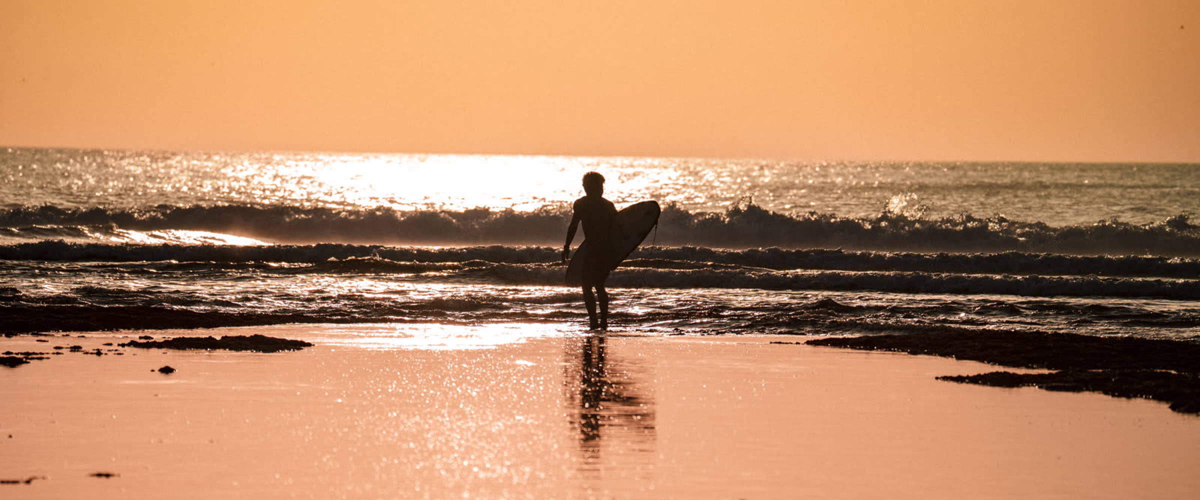 Surfer walking out of the water at golden hour